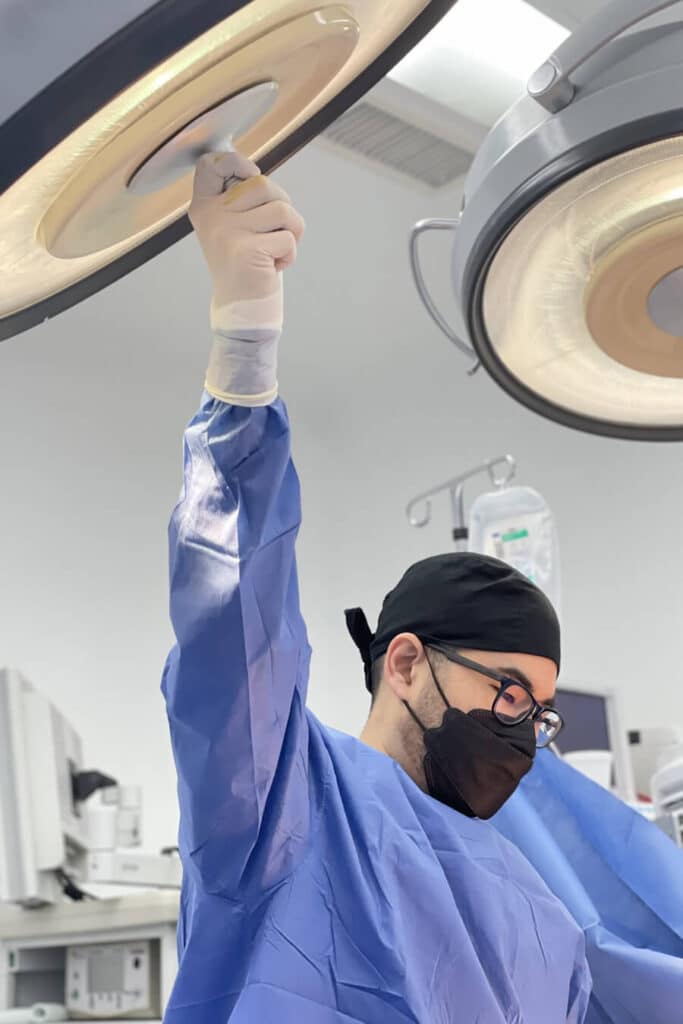 A man in surgical garb and safety glasses working in a clinical setting.
