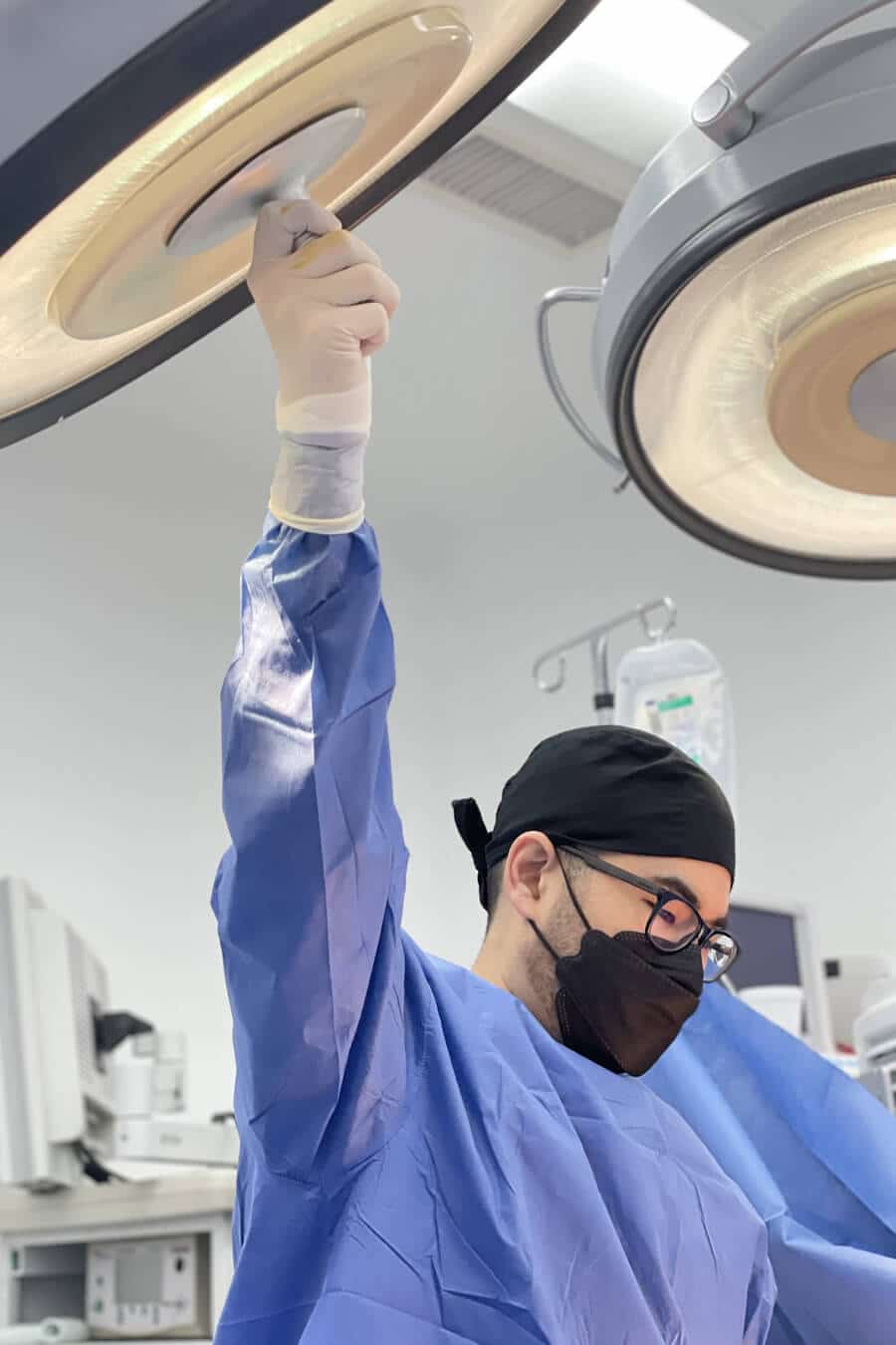 A man in surgical garb and safety glasses working in a clinical setting.