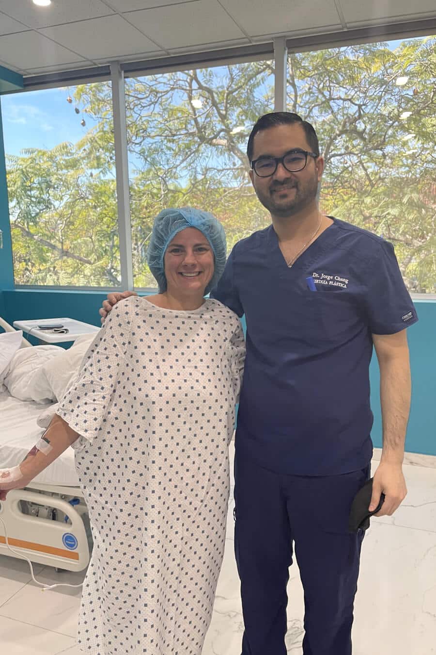 A woman and a man in clinical clothing, both smiling, posing with a grateful-looking patient.