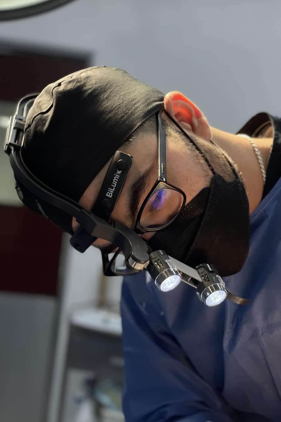 A man in surgical garb and safety glasses focused on his work, possibly during a surgical procedure.