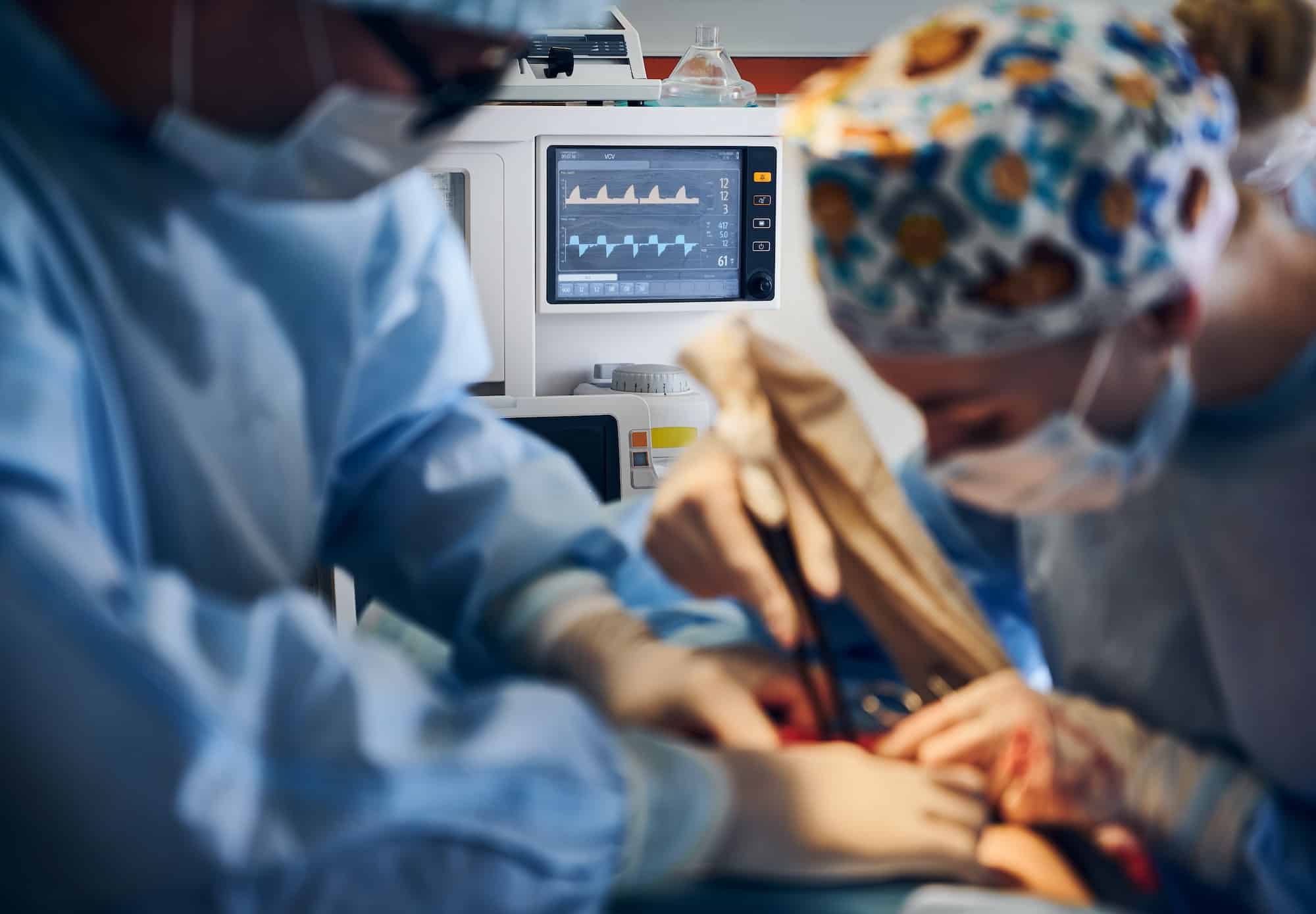 Doctors doing plastic surgery in operating room with patient monitor.