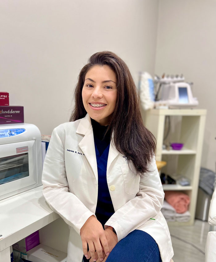 Dr. Gabriela Ruiz, smiling in a lab coat, seated in a medical office.